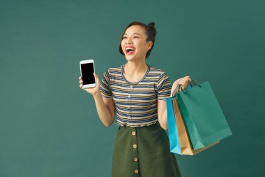 Mutlu Asyalı kadın gülümseyen yüzlü arka plan alışveriş merkezleri olan akıllı telefonu kullanıyor.