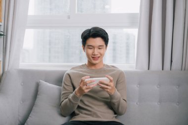 Mutlu genç adam koltukta dinleniyor ve cep telefonuna bakıyor.