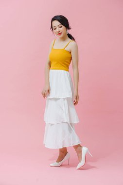 Sarı atlet ve beyaz etekli, uzun saçlı Asyalı genç bir kızın tam boy fotoğrafı. pembe arkaplanda.