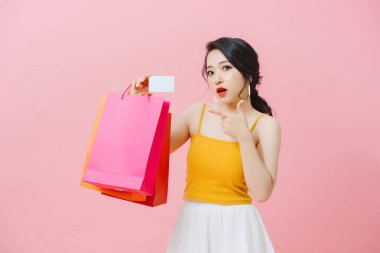 Pembe arka planda soyutlanmış, alışveriş torbaları taşıyan, kredi kartı gösteren sıradan kıyafetler giyen güzel bir genç kız.