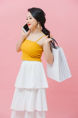 Beyaz arka planda alışveriş torbaları ve cep telefonu tutan mutlu genç bir kadın.