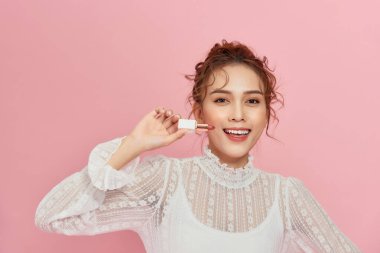 Güzel genç bir kadın pembe ruj sürüyor.