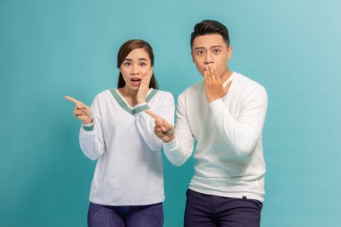Heyecanlı genç çift, iki arkadaş, mavi arka planda yalnız poz veren erkek kız, işaret parmağı bir yana.
