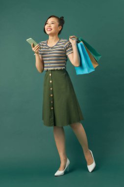 Yeşil arka planda izole edilmiş alışveriş torbaları taşıyan heyecanlı, genç bir kadının fotoğrafı..