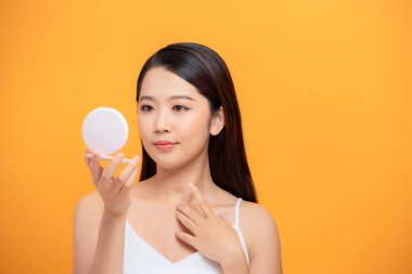 Sarı arka planda izole edilmiş aynaya bakarken yüzünü inceleyen neşeli ve çekici bir kadının güzel portresi.