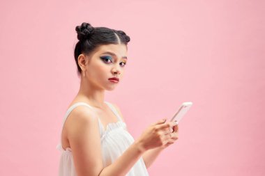 Pembe duvar arkasında cep telefonu kullanarak izole edilmiş mutlu ve iyimser genç bir kadının görüntüsü.