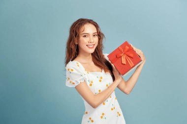 Mutlu gülümseyen bir kızın portresi. Elinde hediye kutusu ve mavi arka planda izole edilmiş göz kırpan bir kız.