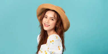 Havalı bir kadın yaz şapkası takıyor kameraya bakıyor ve gülümsüyor, mavi stüdyo arka planında poz veriyor..