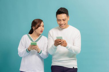 Genç adam ve kadın cep telefonlarıyla yazı yazıyorlar. Kadın erkek arkadaşının telefonuna bakıyor.