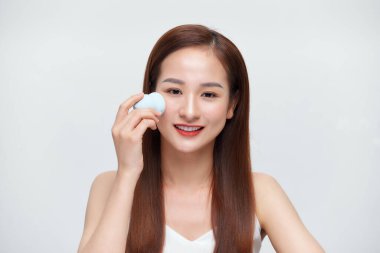 Beyaz arka planda izole edilmiş makyaj süngerleriyle makyaj yapan genç bir kadının portresi.