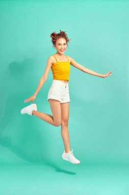 Neşeli genç Asyalı bir kadının açık yeşil arka planda zıplaması..