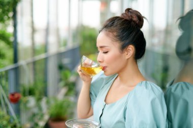 Güzel Asyalı kadın balkonda sabah çayı içiyor.