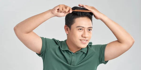 smiling young man brushing hair with comb on white background