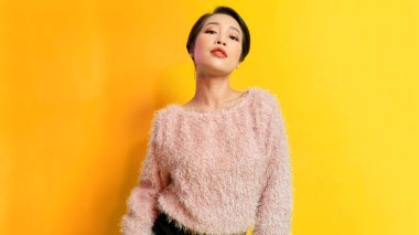 Sarı arka planda poz veren modaya uygun bir genç kadın portresi..