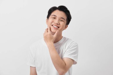 Mutlu ve şaşkın Asyalı genç adam yüzüne dokunuyor, beyaz arka planda beklenmedik bir terfi ile şok oldu.