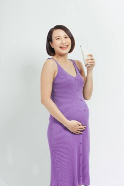 Mutlu hamile kadın bir bardak taze süt içiyor ve özenle karnına dokunuyor.