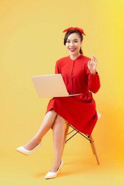 Mutlu genç Asyalı kadın turuncu arka planda dizüstü bilgisayar kullanıyor..