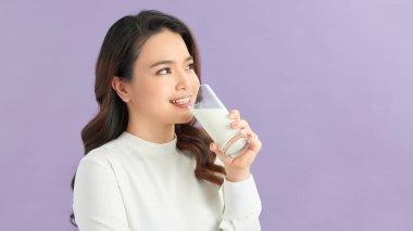 Genç, güzel bir kız elinde süt bardağıyla mutlu bir şekilde mor arka planda kameraya bakıyor.