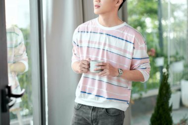 Sabahları pencerenin yanında bir fincan kahvesi olan mutlu yakışıklı bir adam.