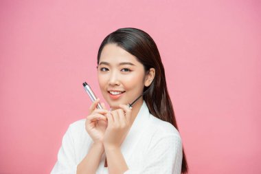 Kirpiklerine siyah maskara sürmüş bir kadın. Pembe arka plan üzerinde fırça ve fotokopi alanı var.