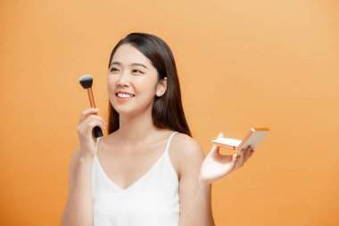 Güzel, genç, esmer bir kadın makyaj fırçası ve küçük bir ayna kullanarak yanağına allık sürüyor.