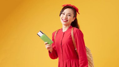 Sarı arka plandan önce pasaportu, uçak bileti ve pasaportu olan neşeli bir kız.,