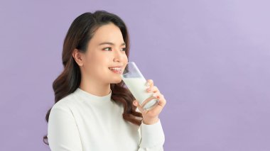 Tatlı, sağlıklı bir kadın leylak arkaplanından izole edilmiş bir bardaktan süt içiyor..