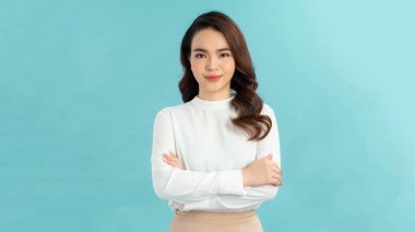 Mavi arka planda kolları çapraz dururken kameraya gülümseyen basit tişörtlü neşeli bir kadın görüntüsü