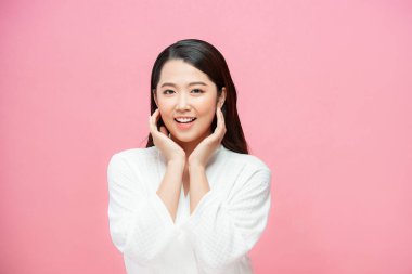 Yanaklarına dokunan ve pembe arka planda kameraya bakan güzel, genç esmer kız portresi.