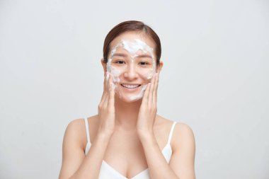 Neşeli Asyalı kadın köpük temizleyici sürüyor, temiz ve sağlıklı bir cildi var..