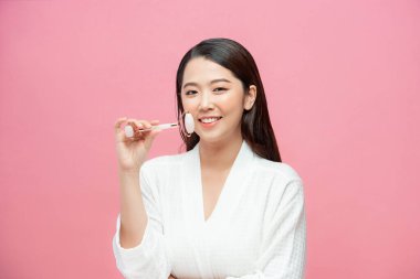 Güzellik yüz bakımı. Açık pembe arka planda doğal masaj aleti portresi kullanan kız