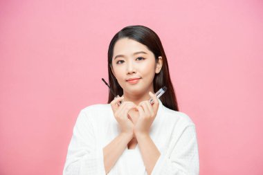 Kirpiklerine siyah maskara sürmüş bir kadın. Pembe arka plan üzerinde fırça ve fotokopi alanı var.