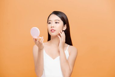 Sarı arka planda izole edilmiş aynaya bakarken yüzünü inceleyen mutlu ve çekici bir kadının güzel portresi.