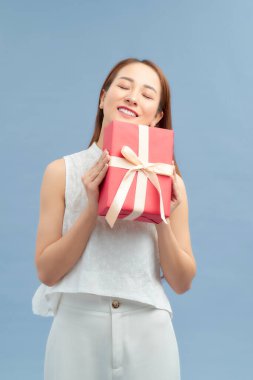 Mavi arka planda izole edilmiş hediye kutusunu tutan mutlu bir kızın portresi.