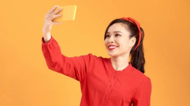 Gülümseyen genç kız sarı arka planda akıllı telefondan selfie çekiyor.