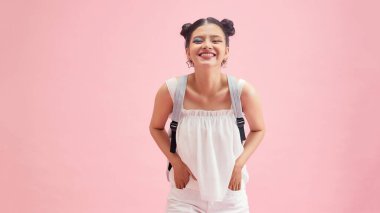 Okul çantasıyla gülümseyen bir kız öğrenci pembe arka planda izole edilmiş.