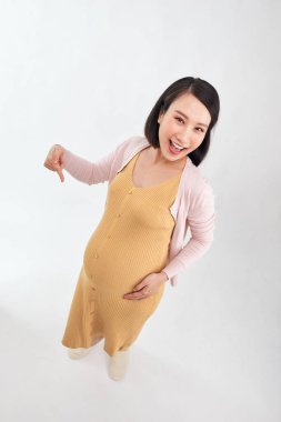 Beyaz arka planda mutlu genç hamile bir kadın, kadın göbeğini işaret ediyor.