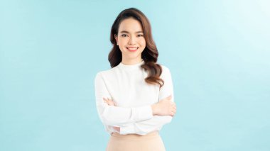 Mavi arka planda kolları çapraz dururken kameraya gülümseyen basit tişörtlü neşeli bir kadın görüntüsü