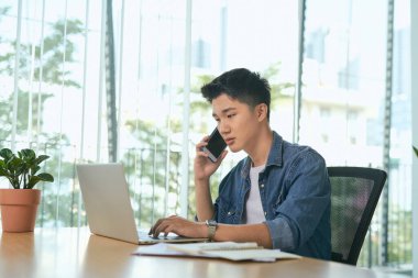 Gülümseyen adam telefon ederken notlar yazıyor ve evde dizüstü bilgisayar kullanıyor.