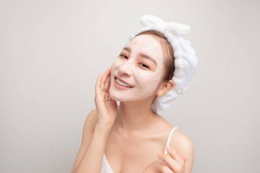 Tatlı bir genç kız spa tedavisinden zevk alıyor, yüzüne kilden bir maske takıyor, gülümsüyor.