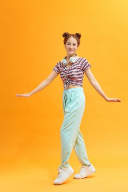 Sarı arka planda izole bir şekilde atlayan neşeli, sıradan Asyalı bir kadının tam boy portresi.