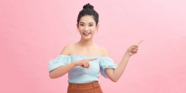 Neşeli genç bir kadın pembe arka plana bakıyor ve onu işaret ediyor..