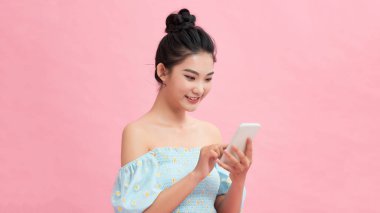 Yepyeni akıllı telefonunu inceliyor. Güzel genç kadınlar ellerinde akıllı telefonlar ve pembe arka planda dururken gülümsüyorlar.