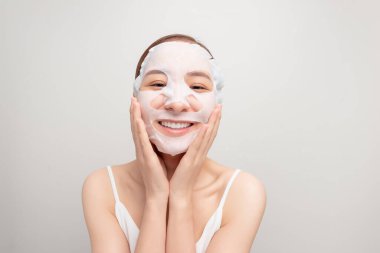 Kafasına havluyla bağlanmış genç bir kadın yüz nemlendirici maske takıyor.