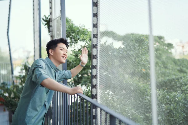 Handsome man leaning on rail, waving from balcony,