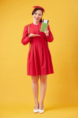 Smiling young woman tourist with backpack holding passport and flight tickets, yellow studio background