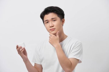 beauty, skin care and people concept - smiling young man with cream jar on gray background