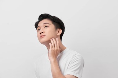 Yakışıklı bir adam yüzüne dokunuyor. Beyaz arka planda portre stüdyosunu kapatıyor.