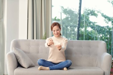 Güzel, güzel bir kız kanepeye oturmuş cep telefonu kullanıyor ve online video oyunu oynuyor.