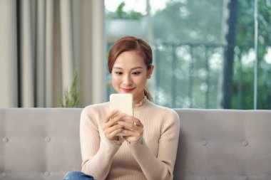 Genç Asyalı kadın odada akıllı telefon kullanıyor..